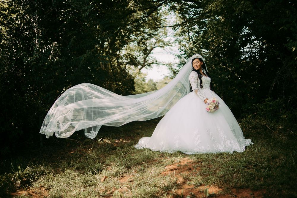 A bride in a flowing white wedding dress poses gracefully on a grassy hill during a romantic outdoor photo session.