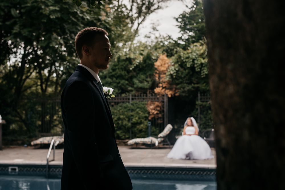 A couple in wedding attire walks together through a lush garden setting during an autumn day.